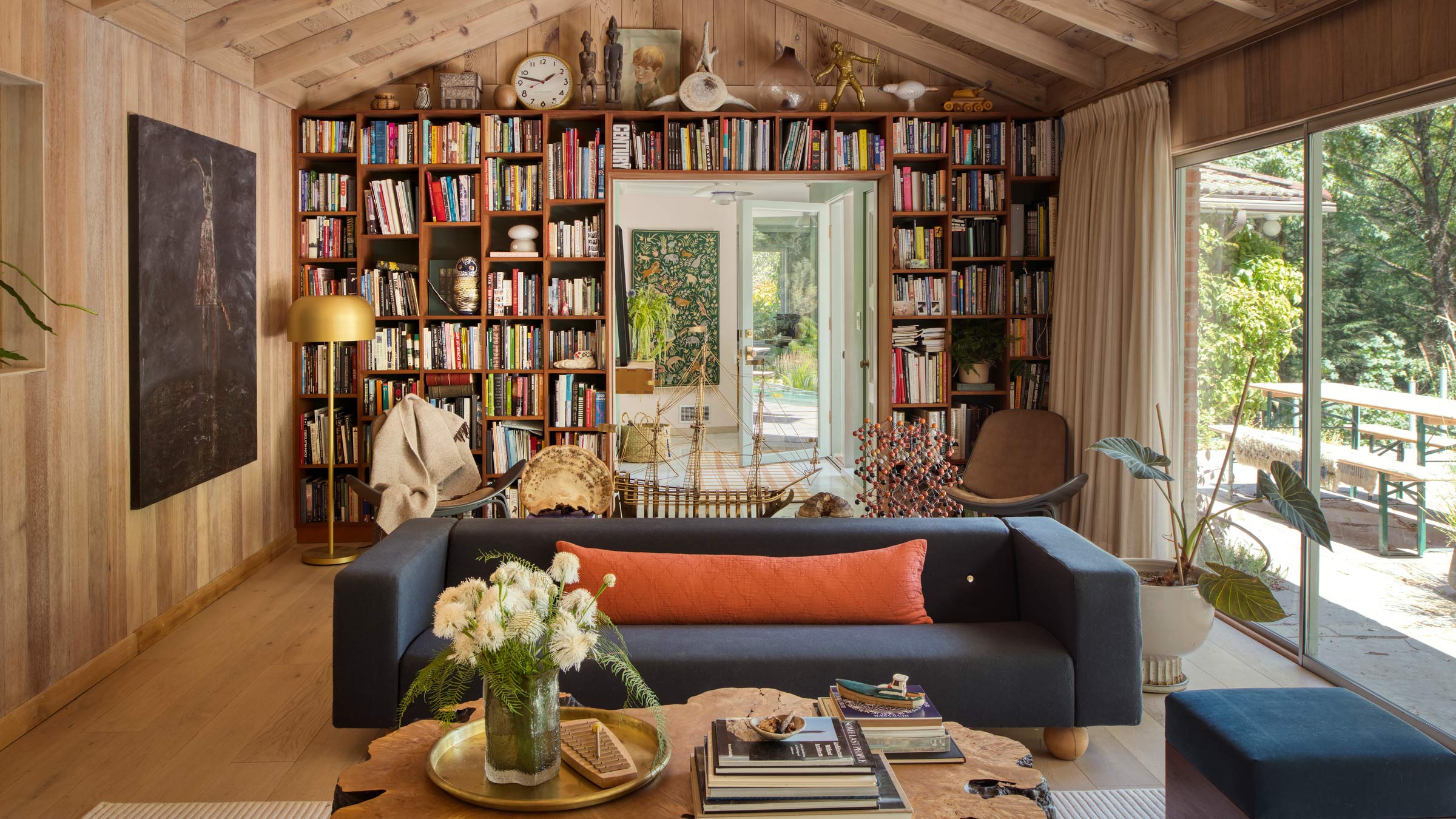 Cozy living room with built-in bookshelves behind a navy sofa, coffee table with books and flowers, glass doors to a sunlit patio