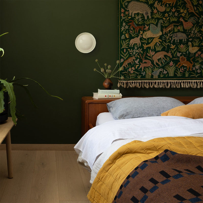 Bed with white sheets, grey pillowcases, and brown blanket in dark green room